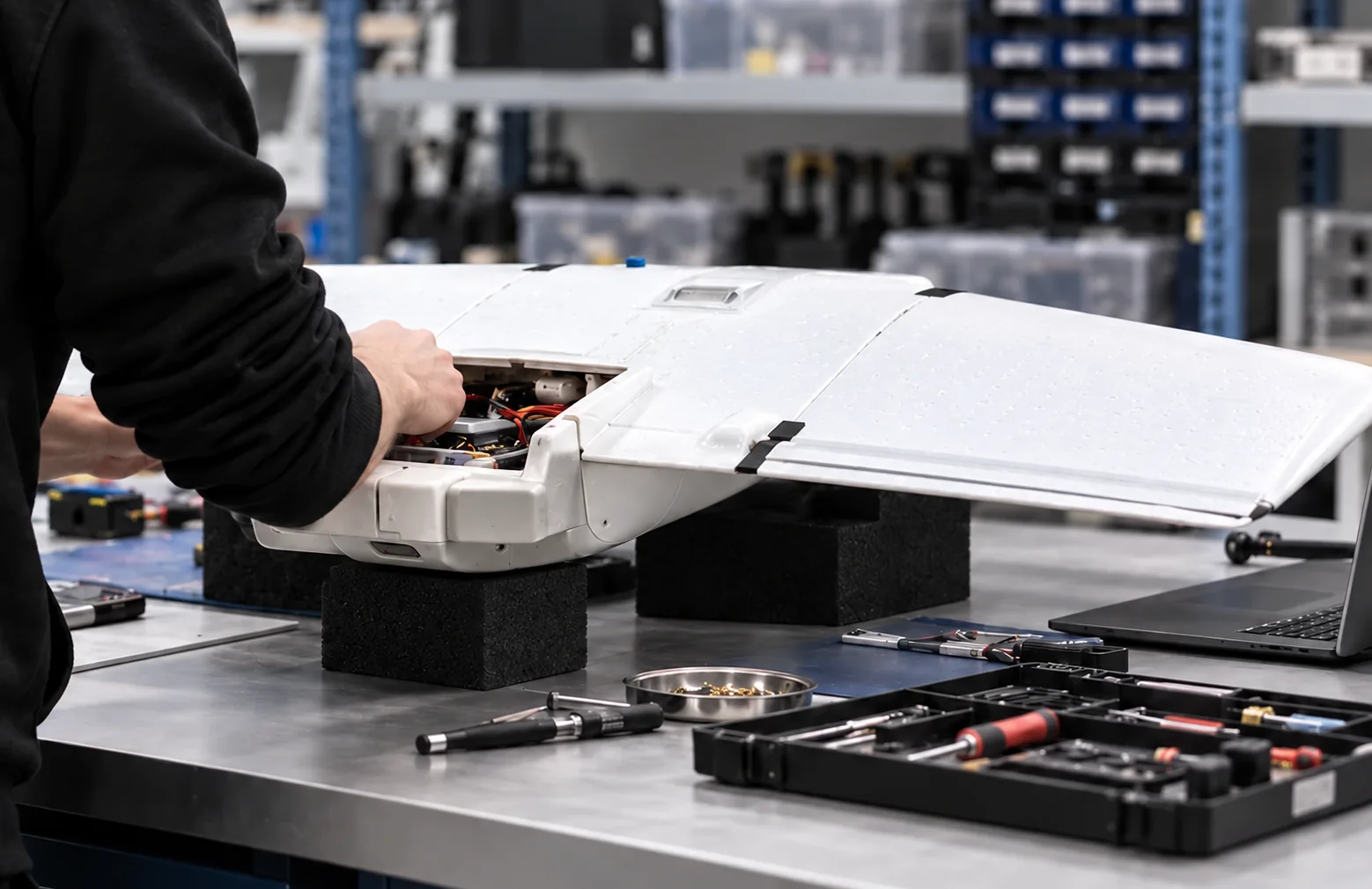 A UAVSAVE technician checks the exposed electronics inside a white fixed-wing UAV in the workshop
